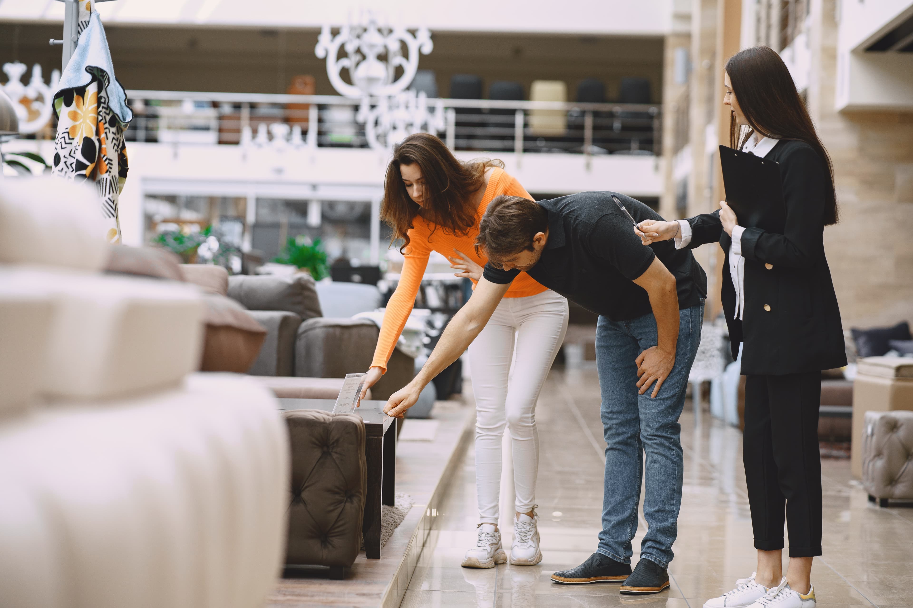 Couple inspects a coffee table in a furniture store while a saleswoman stands nearby.