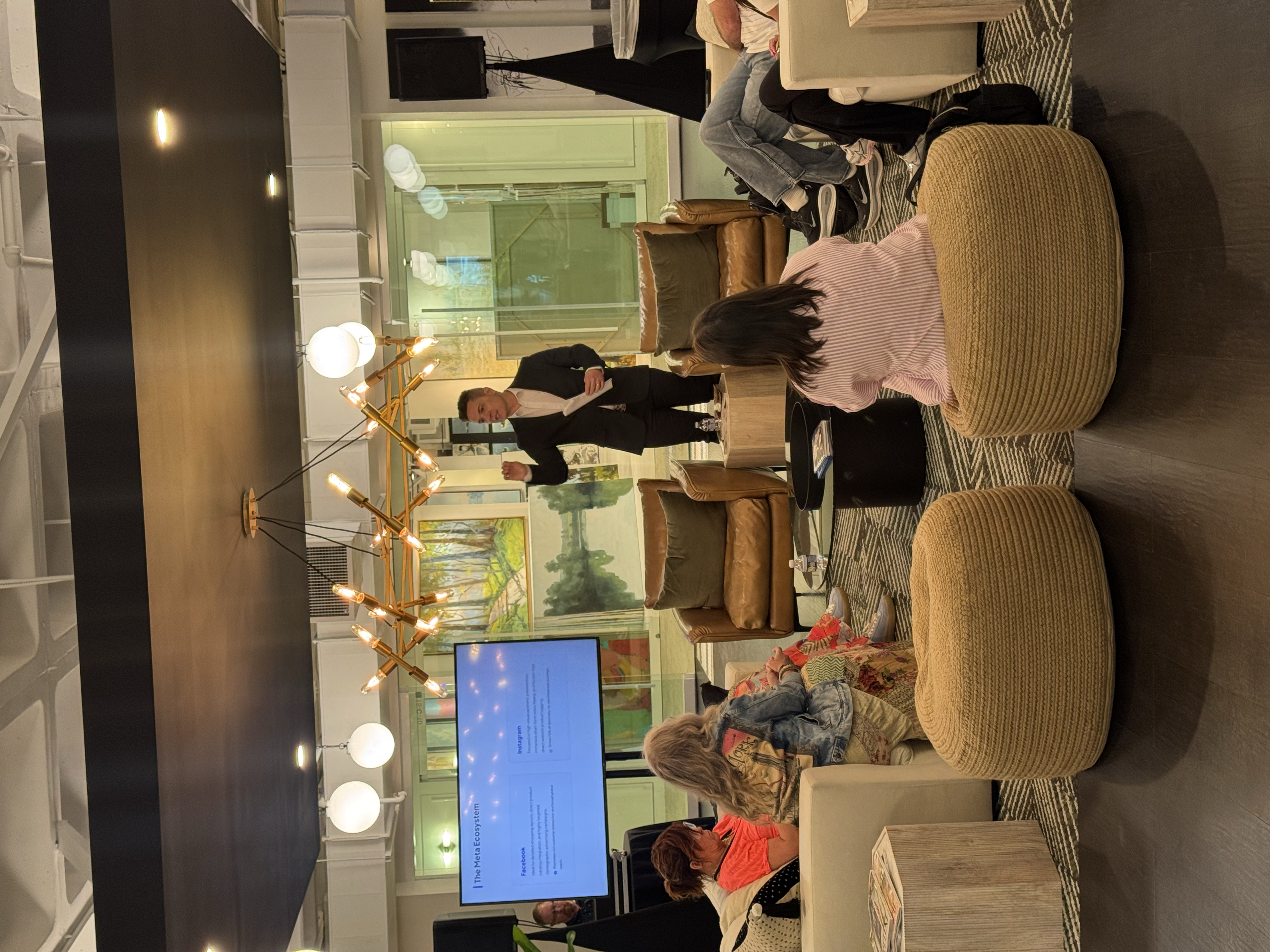 Man in a suit presenting to a small group in a modern, stylishly decorated lounge.