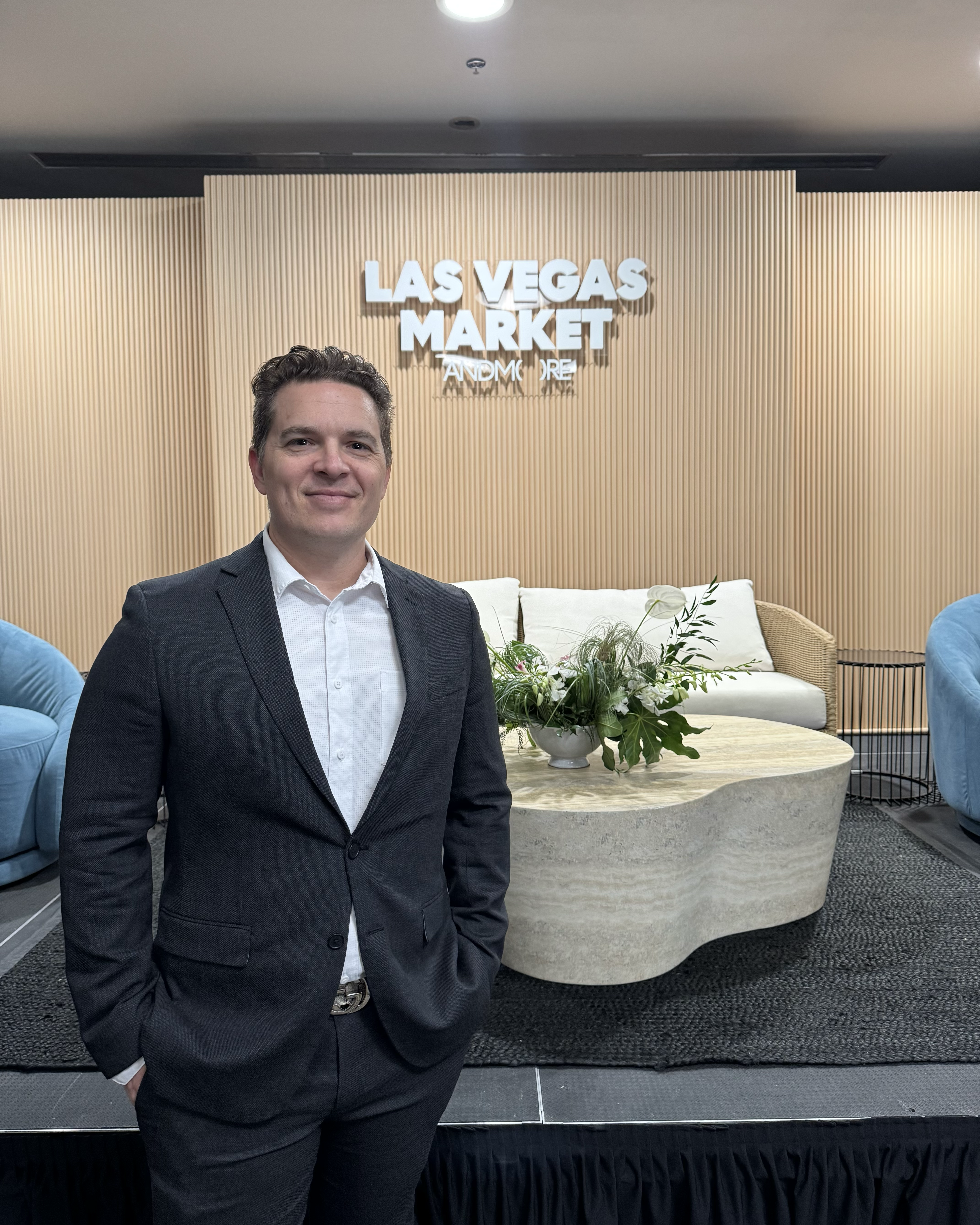 Man in a suit standing before a Las Vegas Market sign in a modern showroom.